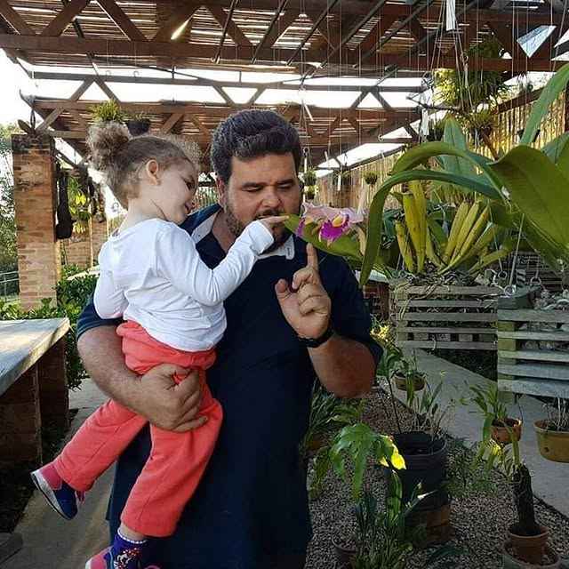 Demis Lima com uma criança no colo observando uma orquídea